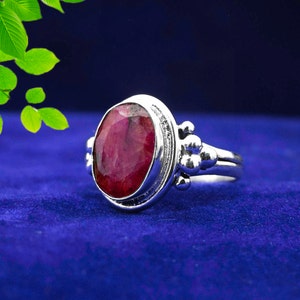 May include: A silver ring with a large, oval-shaped ruby gemstone. The ring has a decorative band with small, round accents.