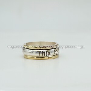 K&ouml;nnte beinhalten: Ein drehbarer Ring aus Silber und Gold mit der Gravur "This too" auf dem Band.