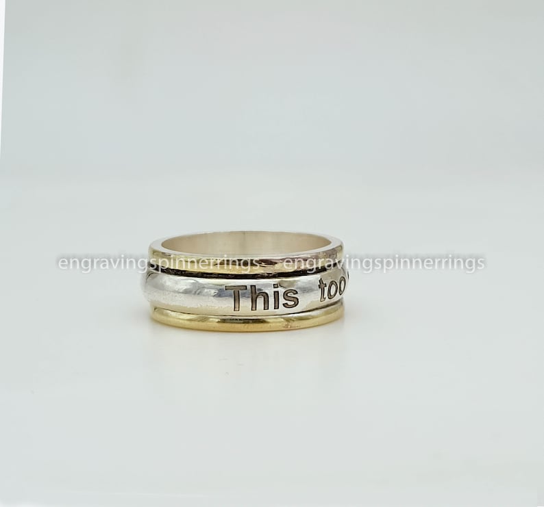 K&ouml;nnte beinhalten: Ein drehbarer Ring aus Silber und Gold mit der Gravur "This too" auf dem Band.
