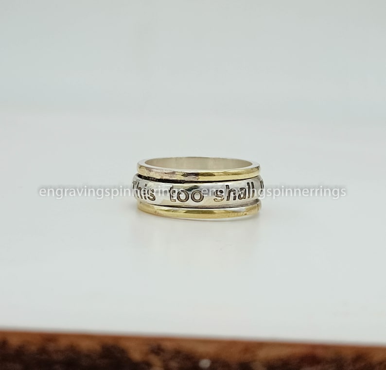 K&ouml;nnte beinhalten: Ein drehbarer Ring aus Silber und Gold mit der Gravur "This too shall pass".