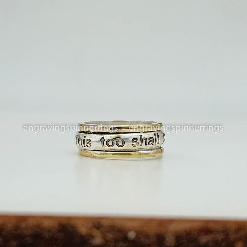 K&ouml;nnte beinhalten: Ein drehbarer Ring aus Silber und Gold mit der Gravur "this too shall".
