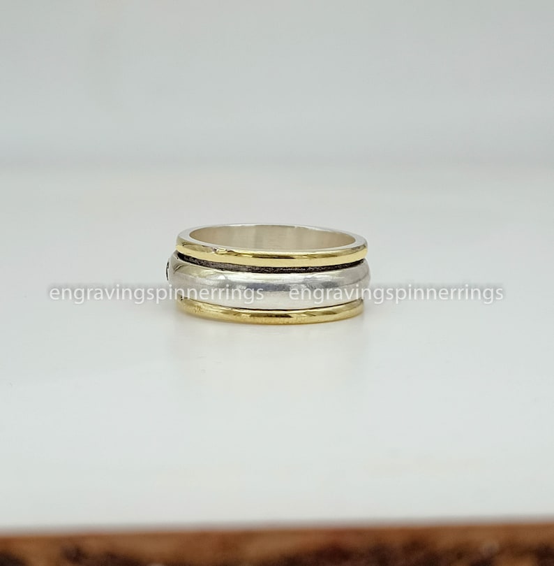 K&ouml;nnte beinhalten: Ein dreireihiger Spinnerring aus Silber und Gold. Der Ring ist aus Metall und hat eine glatte Oberfl&auml;che.