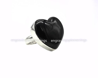 Può includere: Un anello d'argento con una grande pietra nera lucida a forma di cuore. L'anello ha una fascia larga e un'incastonatura a castone. La pietra a forma di cuore è su sfondo bianco.
