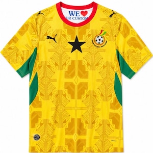 Op de afbeelding: Een geel shirt met korte mouwen, een zwarte ster in het midden, groene zijpanelen en een rode kraag. Het shirt toont het logo van de Ghana Football Association, Puma-branding en een herhalend geometrisch patroon. Het binnenlabel bevat de tekst WE LOVE OUR CUSTOM.