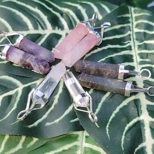 Pode incluir: Seis pingentes de ponta de cristal com engastes de prata. Os cristais são transparentes, rosa, roxo e cinza.