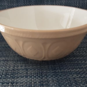 May include: A beige ceramic mixing bowl with a white interior. The bowl has a rounded shape with a decorative embossed pattern around the exterior. The rim is slightly flared. Ideal for baking and cooking.