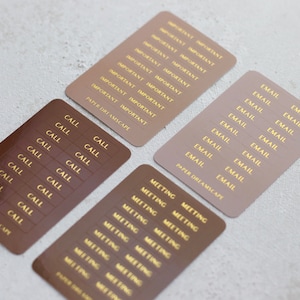 Puede incluir: Conjunto de 10 pegatinas de planificador de papel marrón y beige con letras doradas. Las pegatinas incluyen las palabras "Llamar", "Correo electrónico", "Reunión" e "Importante".