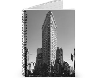 May include: Black and white photograph of the Flatiron Building in New York City. The building is a triangular skyscraper with a distinctive pointed roof.