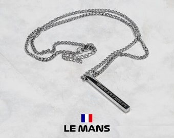 Puede incluir: Collar plateado con un colgante rectangular con coordenadas grabadas, suspendido de una cadena de eslabones. La palabra "LE MANS" está debajo del colgante, junto con la bandera francesa.