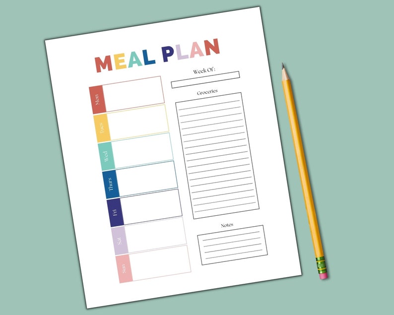 May include: A white paper meal plan with the words "MEAL PLAN" in colorful letters. The days of the week are listed in color-coded boxes. A yellow pencil with a pink eraser rests on the right side of the paper.
