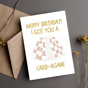 May include: A white card with gold text that reads "Happy Birthday! I got you a card-again!" and a cartoon image of a pink and white checkered cardigan.