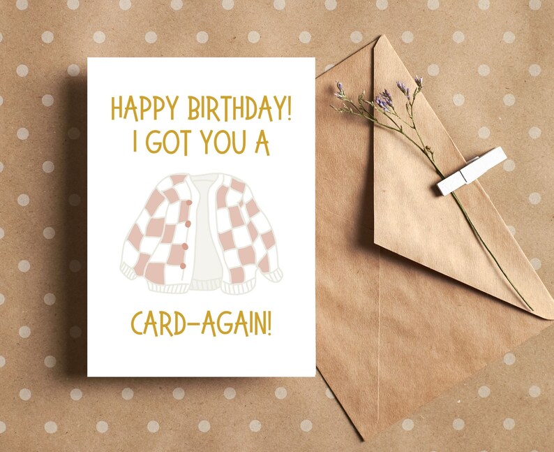 May include: A white card with the text "Happy Birthday! I got you a card-again!" in gold lettering. A pink and white checkered cardigan is illustrated in the center of the card.
