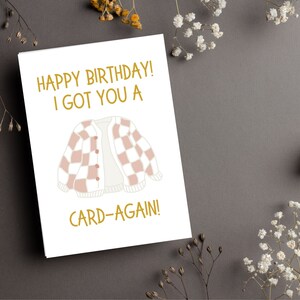 May include: A white card with gold text that reads "Happy Birthday! I got you a card-again!" and a pink and white checkered cardigan illustration.