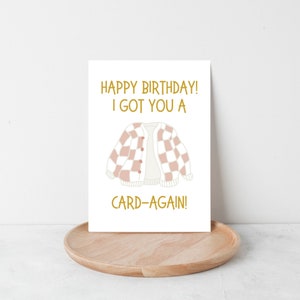 May include: A white card with gold text that reads "Happy Birthday! I got you a card-again!" and a pink and white checkered cardigan illustration.