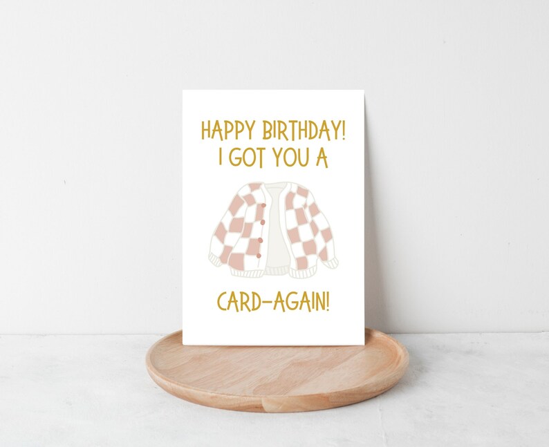 May include: A white card with gold text that reads "Happy Birthday! I got you a card-again!" and a pink and white checkered cardigan illustration.