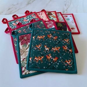 Peut inclure: Une collection de maniques matelassées sur le thème de Noël. Les motifs comprennent des rennes, des poinsettias et des motifs festifs. Chaque manique a une bordure contrastante et une boucle pour suspendre. Les couleurs sont principalement rouge, vert et blanc.