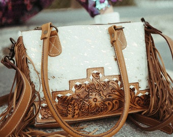 Könnte beinhalten: Eine weiße Ledertasche mit braunen Lederbesätzen und Fransen. Die Tasche hat ein geprägtes Blumenmuster auf der Vorderseite.
