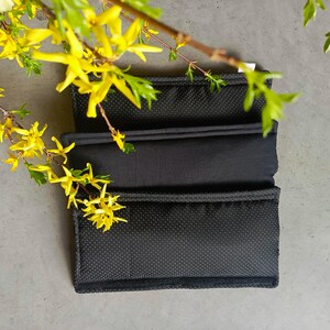 May include: Three black fabric cushions with a textured surface. The cushions are stacked on top of each other.