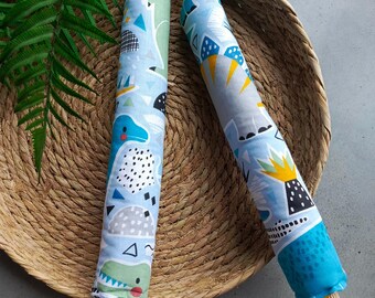 May include: Two wooden dowels wrapped in blue fabric with a dinosaur print. The fabric has a white background with blue, green, yellow, and black dinosaur silhouettes. The dowels are in a woven basket.