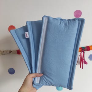 Puede incluir: Tres almohadas rectangulares de color azul claro con costuras blancas y una etiqueta blanca que dice "glitch".