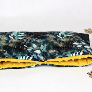 May include: A dark green and gold patterned pillow with a yellow fleece lining. The pillow is folded in half and lying on a white surface.