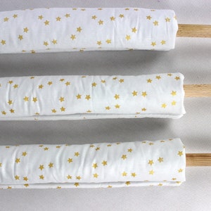 May include: Three white fabric rolls with gold star patterns are rolled around wooden dowels. The fabric is white with gold stars printed on it.