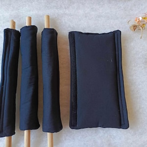 Puede incluir: Tres varillas cubiertas de tela negra con clavijas de madera y un cojín cubierto de tela negra.