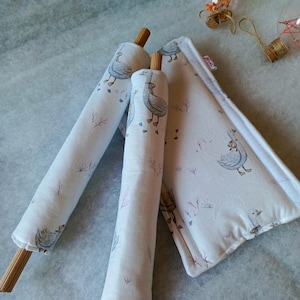 May include: Three white fabric-covered cushions with a goose print design. The cushions are rolled up and have wooden dowels at the ends.