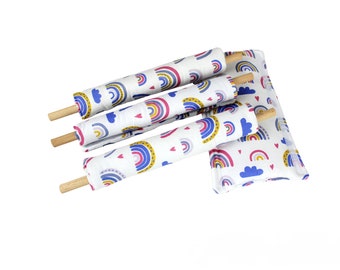 May include: Four rainbow-patterned fabric rolls with wooden dowels and a matching pillow. The fabric features rainbows, clouds, and hearts in shades of pink, blue, yellow, and white.