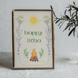 Op de afbeelding: Een gouden ingelijste print met een groene rand en de tekst "happy Litha" in groene letters. De print bevat een zon, een kampvuur en bloemmotieven.