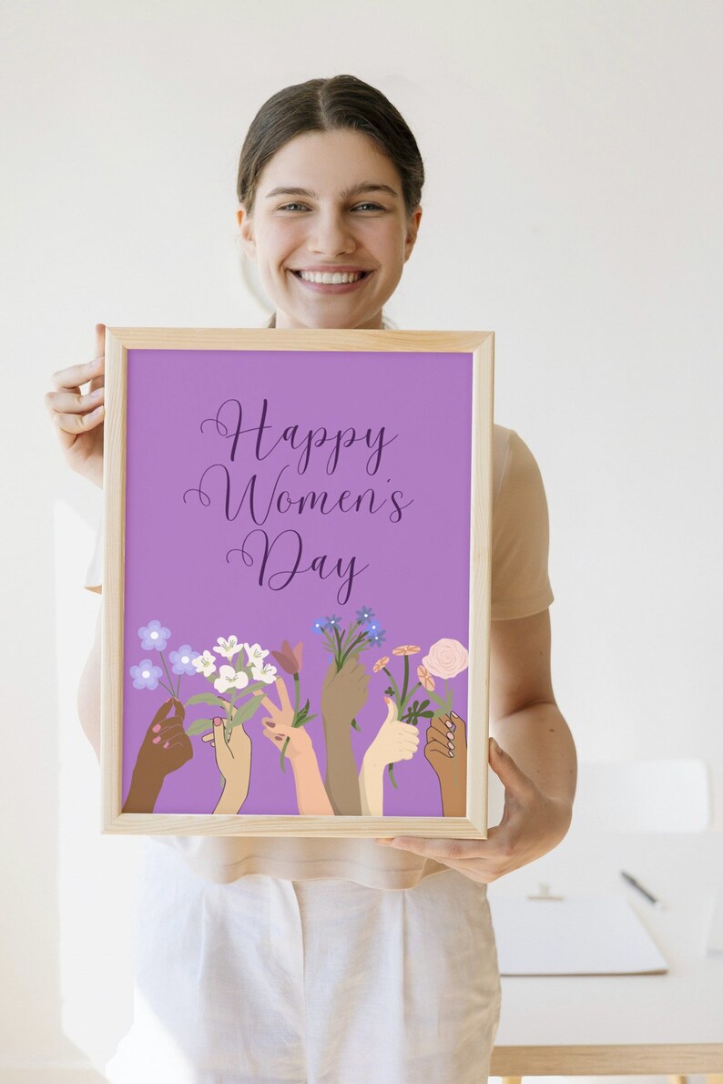 May include: A framed print with a purple background and the text "Happy Women's Day" in a purple script font.  The print features a design of multiple hands of different skin tones holding flowers.