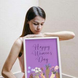 May include: A white framed print with a purple background and the text "Happy Women's Day" in a cursive font.  The print features a series of colorful hands holding bouquets of flowers.