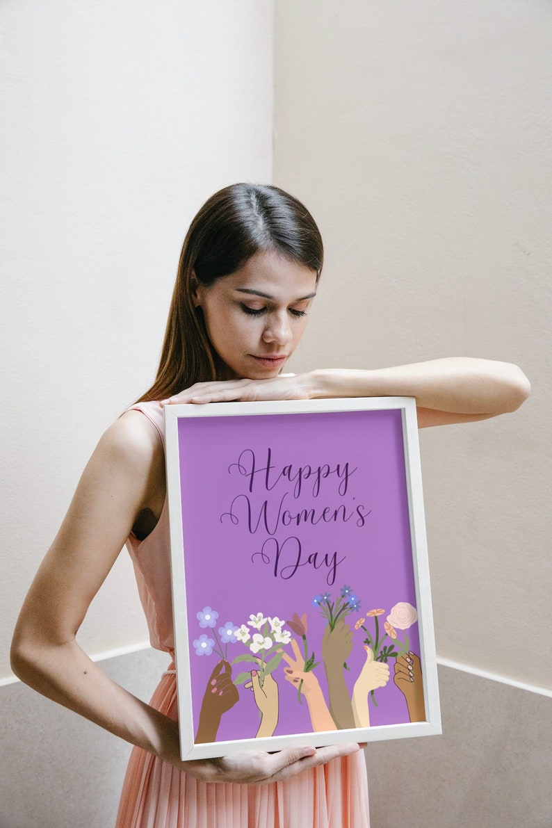 May include: A white framed print with a purple background and the text "Happy Women's Day" in a cursive font.  The print features a series of colorful hands holding bouquets of flowers.