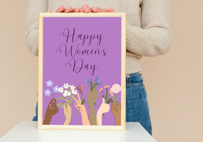 May include: A framed print with a purple background and the text "Happy Women's Day". The print features a variety of hands holding flowers in different colors.