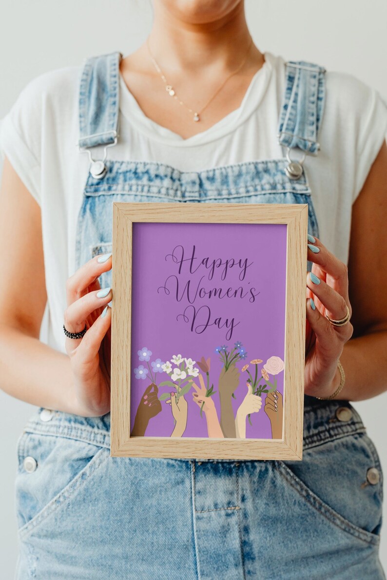May include: A framed print with a purple background and the text "Happy Women's Day". The print features a colorful illustration of hands holding flowers.