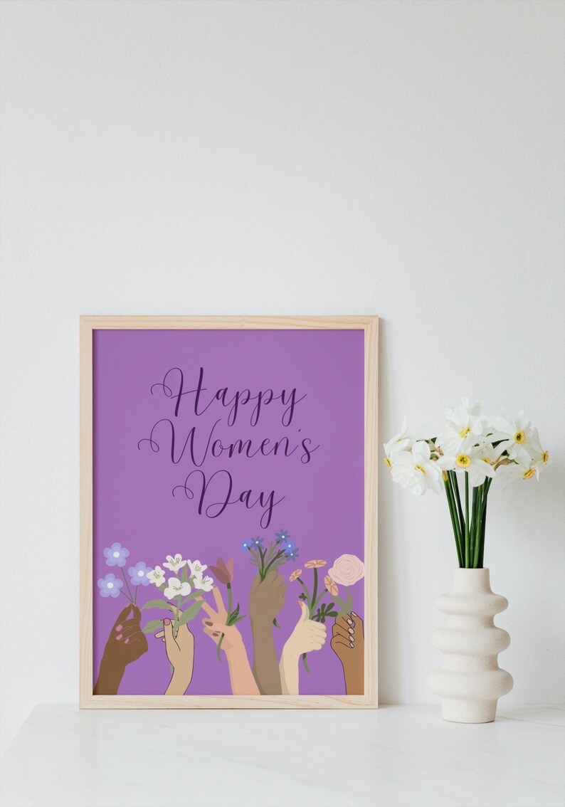 May include: A framed print with a purple background and the text "Happy Women's Day". The print features a row of diverse hands holding flowers.