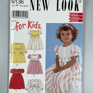May include: A sewing pattern for children's dresses. The pattern includes four different styles: a yellow dress with a sash, a pink dress with a floral print, a red dress with white stars, and a white dress with a Peter Pan collar. The pattern is from New Look and is size 1/2, 1, 2, 3, and 4.
