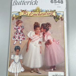 May include: A sewing pattern for three girls' dresses. The pattern is called "It's Enchanting" and is from Butterick. The pattern number is 6548 and the sizes are 2-3-4. The dresses are all white with different embellishments. The dress on the left has a floral print, the dress in the middle has a white sash, and the dress on the right has a pink sash.