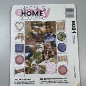 May include: A McCall's Home Decorating sewing pattern envelope for 8081 Pillow Essentials. The white paper envelope features a central photograph of ten various decorative pillows in plaid, solid, and ruffled designs, with text and a barcode.