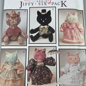 Könnte beinhalten: Ein Simplicity-Schnittmuster zum Nähen von sechs Plüschkatzenspielzeugen. Das Schnittmuster enthält Anleitungen zum Nähen einer Cowboykatze, einer Tuxedo-Katze, einer Katze in einem rosa Kleid, einer Katze in einem Blumenkleid, einer Katze in einem blauen Kleid und einer Katze in einem weißen Kleid. Das Schnittmuster trägt den Titel "Jiffy Six Pack".