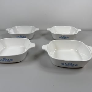 May include: Four white square casserole dishes with handles. Each dish has a blue floral design on the front. The dishes are made of a durable material and are suitable for baking and serving.