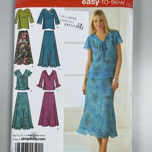 May include: A sewing pattern for a women's top and skirt. The pattern is for sizes 10, 12, 14, 16, and 18. The pattern includes instructions for making a top with a V-neck and short sleeves, and a skirt with a frilled hem. The pattern is from Simplicity and is easy-to-sew.