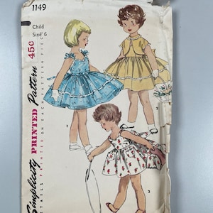 Peut inclure: Patron de couture vintage Simplicity pour une robe d'enfant. Le patron est pour la taille 6 et est imprimé sur du papier blanc avec une bordure bleue et jaune. Le patron montre trois filles portant différentes robes. Le numéro du patron est 1149 et le prix est de 45 cents.