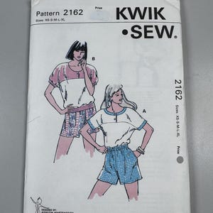 Puede incluir: Un sobre de patrón Kwik Sew para el modelo 2162, con ilustraciones de dos conjuntos etiquetados como A y B. El patrón incluye las tallas XS, S, M, L y XL. La cubierta muestra el nombre de la marca, la dirección y un código de barras.