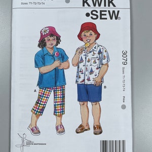May include: Sewing pattern for children's clothing, featuring a girl wearing a blue shirt, plaid trousers, and a pink hat, and a boy wearing a blue and white striped shirt, blue shorts, and a red hat. The pattern is called "Kwik Sew" and the number is 3079. The pattern is for sizes T1-T2-T3-T4.