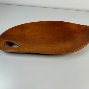May include: A wooden serving tray with a unique, leaf-shaped design. The tray has a cutout handle and a rich brown color.