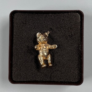 May include: A gold-colored teddy bear charm in a black velvet box. The bear is standing on all fours with its arms outstretched.
