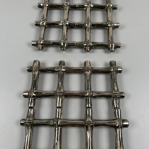 May include: Two silver metal bamboo-style hot pads. The hot pads are made of interwoven metal rods that resemble bamboo.