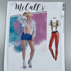 May include: McCall's sewing pattern M8129, size E5 (14-16-18-20-22), featuring a colourful illustration of a woman wearing a cropped jacket, a plaid top, denim shorts, and boots. The pattern also includes a separate illustration of a red jumpsuit with a black top.
