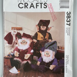 May include: A sewing pattern for three elf dolls. The pattern is from McCall's Crafts and is called "FabricLand". The pattern includes instructions for making the elves, which are dressed in red, green, and purple clothing. The pattern also includes instructions for making the elves' hats and beards.